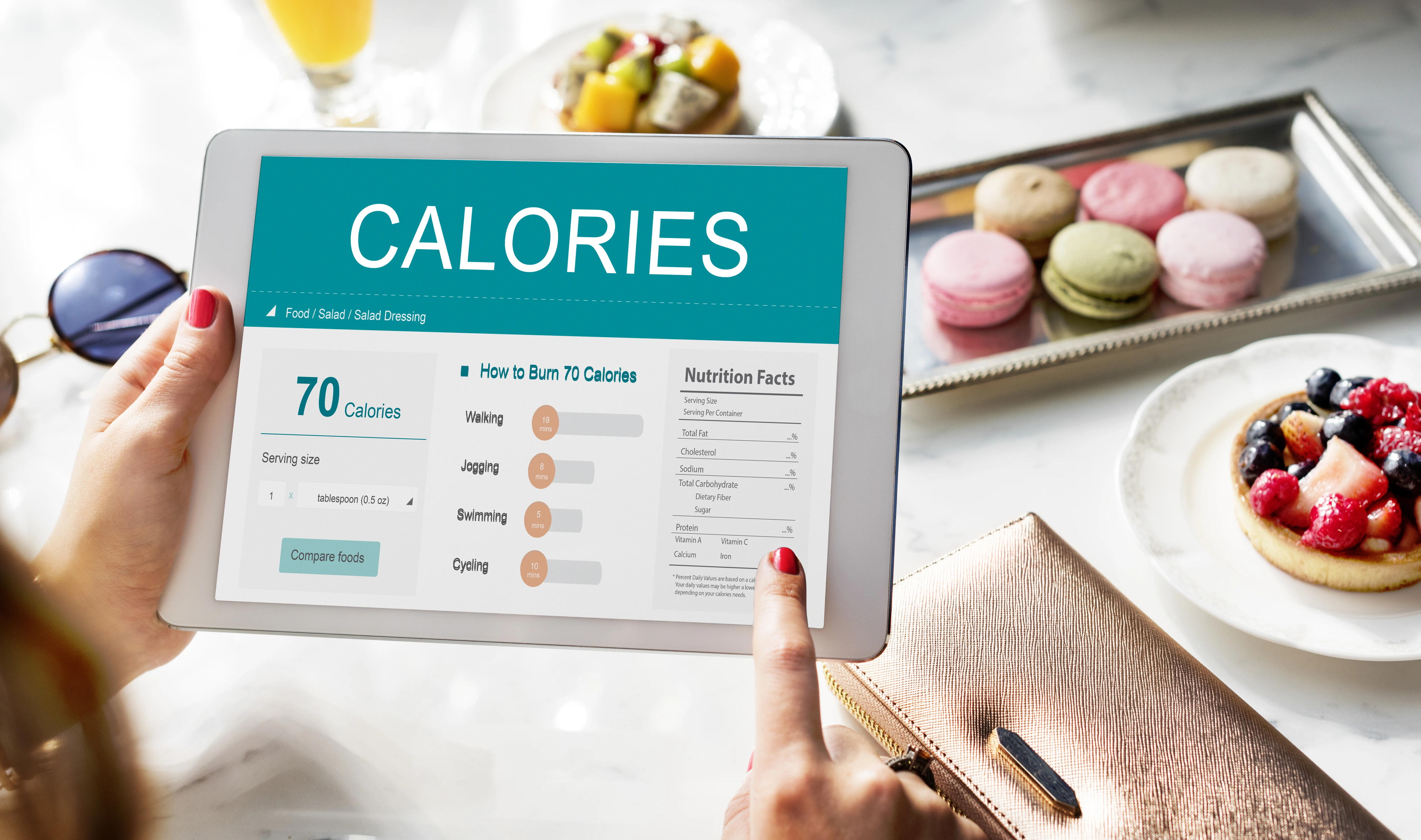 Person using a calorie Bmi calculator on a tablet with nutrition info and desserts in background
