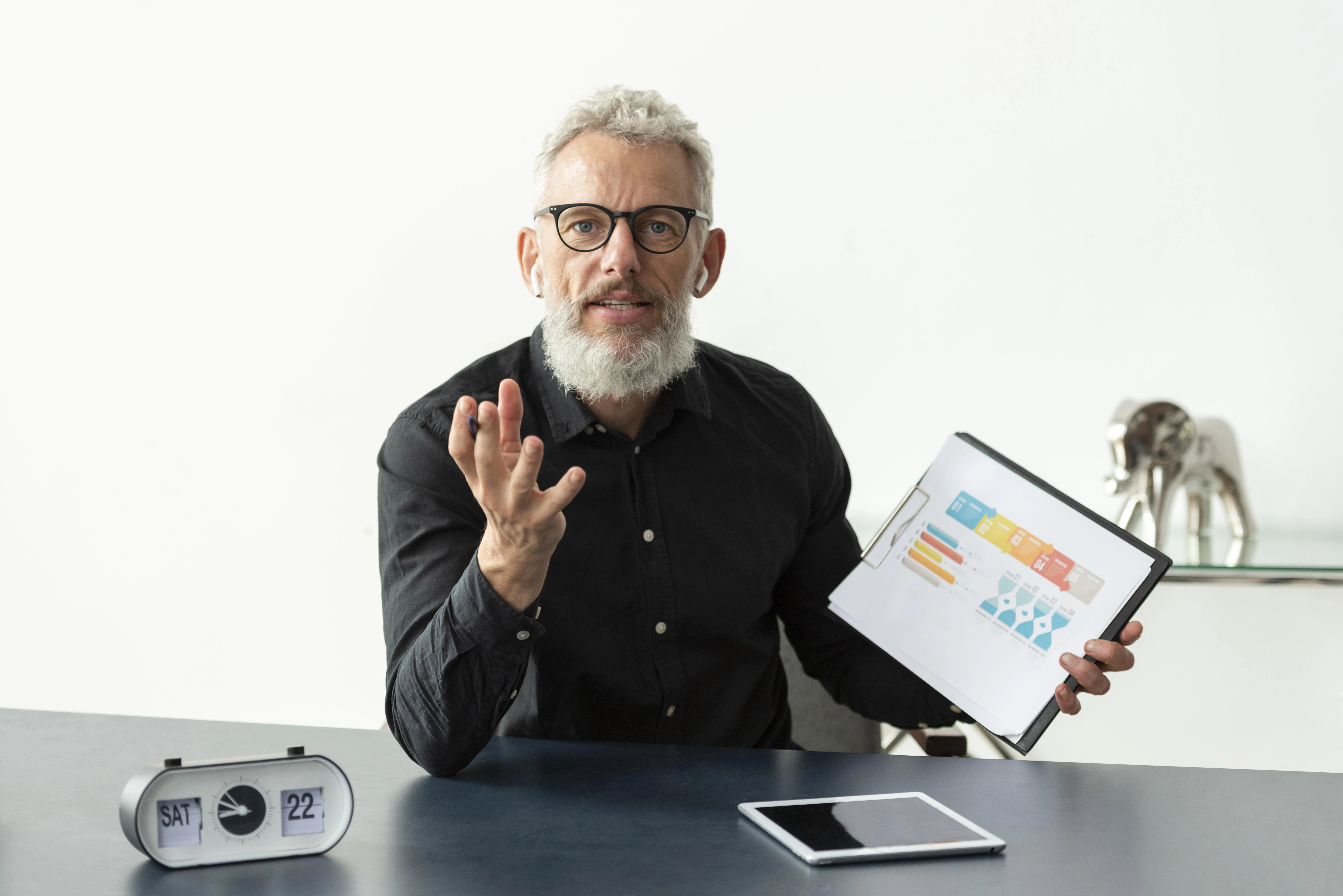 Older man showing online age calculation graph on notepad with clock and tablet